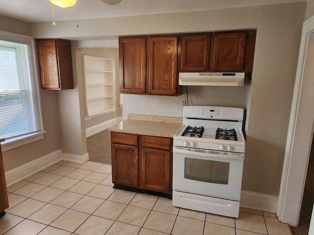 kitchen with light tile patterned floors, baseboards, gas range gas stove, light countertops, and under cabinet range hood