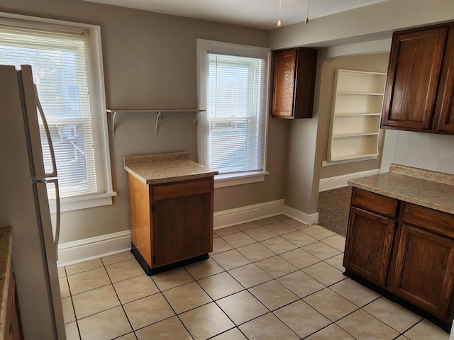 kitchen with light tile patterned floors, a healthy amount of sunlight, freestanding refrigerator, and baseboards