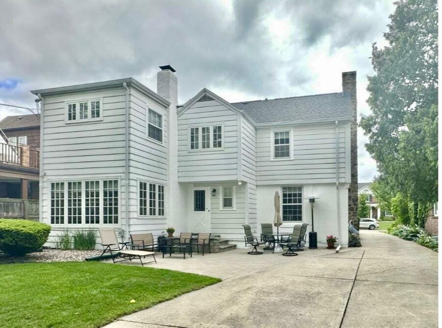 back of house with entry steps, a patio area, a lawn, and a chimney