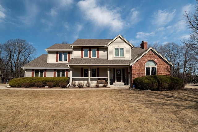 traditional home featuring covered porch, a shingled roof, a chimney, a front lawn, and brick siding