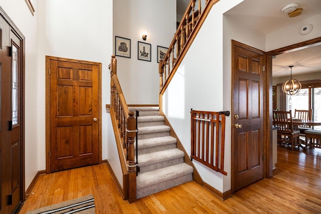 entryway featuring baseboards, a chandelier, stairs, and light wood finished floors