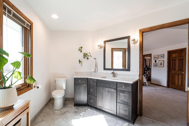 bathroom featuring baseboards, plenty of natural light, toilet, and vanity