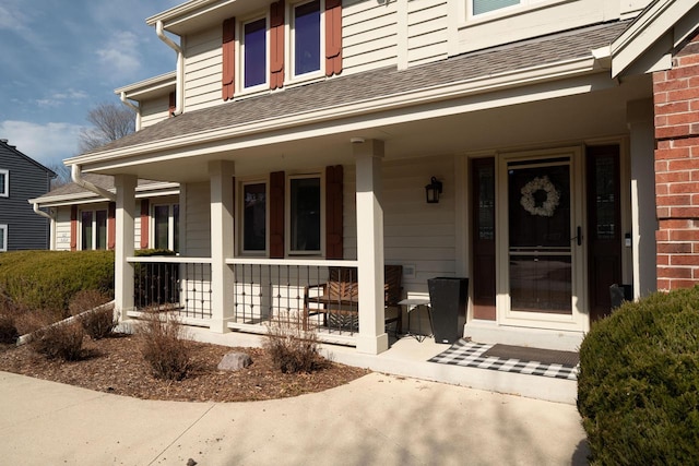 entrance to property featuring brick siding, a porch, and a shingled roof