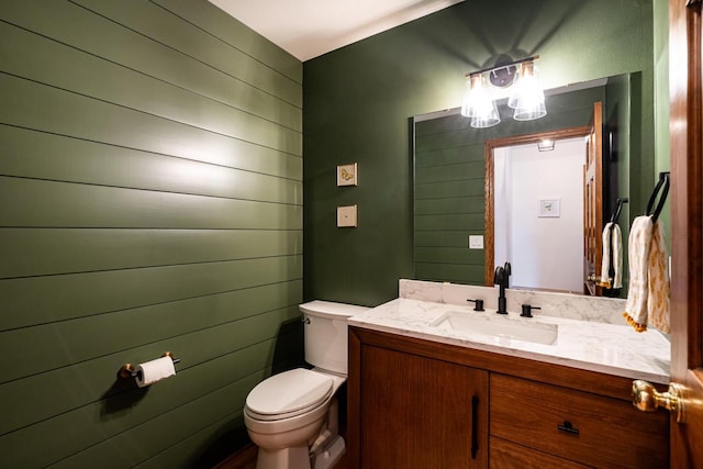 bathroom with wooden walls, toilet, and vanity