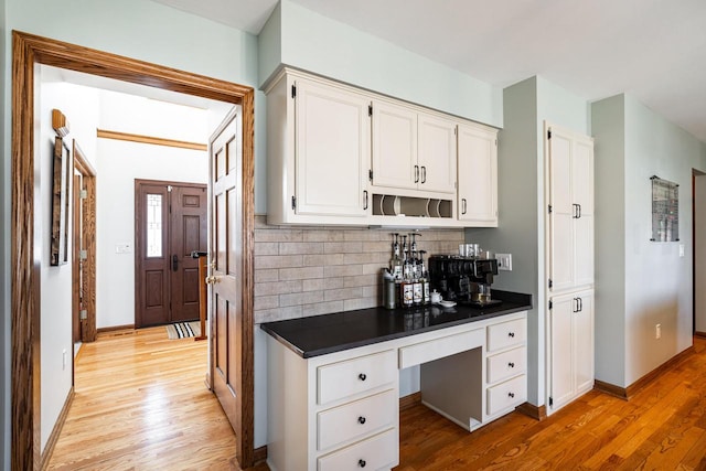 kitchen featuring dark countertops, light wood finished floors, backsplash, and built in study area