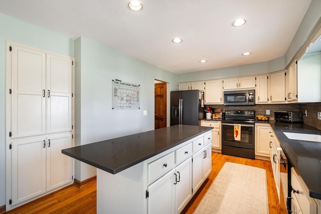 kitchen with a sink, light wood-type flooring, backsplash, and black appliances