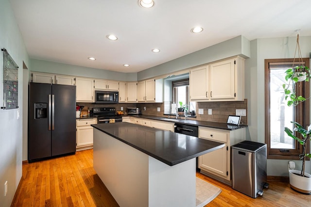 kitchen featuring light wood-style flooring, a sink, decorative backsplash, black appliances, and dark countertops