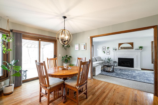 dining space featuring a notable chandelier, a fireplace with raised hearth, and light wood-style floors