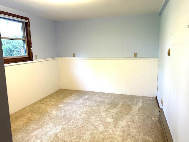 carpeted empty room with a wainscoted wall and a baseboard radiator