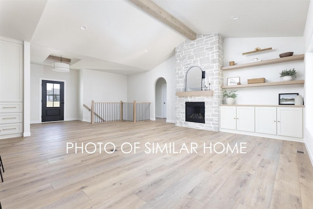 unfurnished living room featuring baseboards, a fireplace, vaulted ceiling with beams, and light wood finished floors