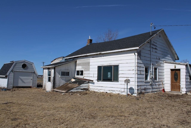 back of house with an outbuilding, a chimney, and a storage unit