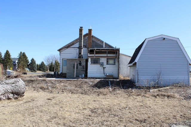 back of house with a gambrel roof, a chimney, and an outdoor structure