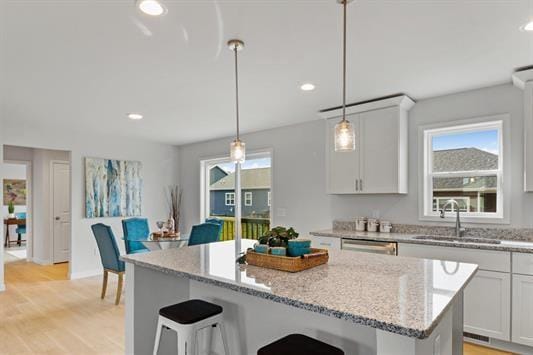 kitchen featuring a sink, a kitchen bar, light stone countertops, and light wood-style flooring