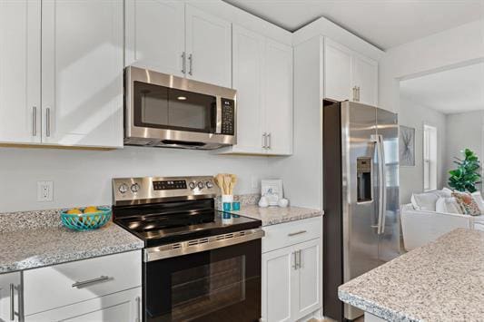 kitchen with light stone counters, white cabinetry, and stainless steel appliances