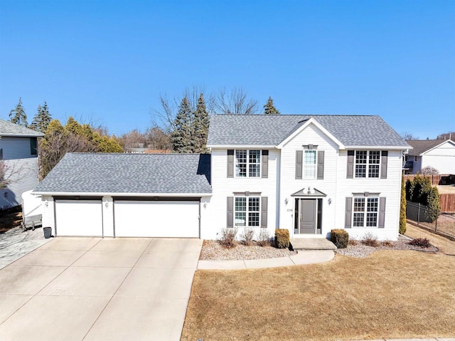 colonial inspired home with fence, a shingled roof, concrete driveway, a front lawn, and a garage