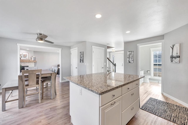 kitchen with light wood-type flooring, light stone counters, a kitchen island, a fireplace, and baseboards