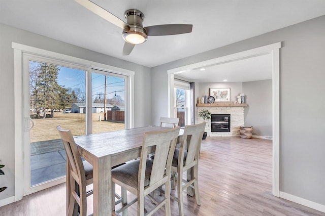 dining space with a stone fireplace, baseboards, and light wood-type flooring