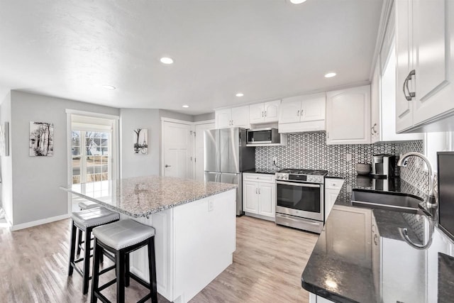 kitchen featuring a sink, a center island, appliances with stainless steel finishes, light wood finished floors, and decorative backsplash