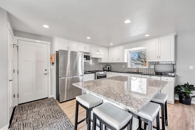 kitchen with a kitchen bar, light wood-type flooring, a sink, tasteful backsplash, and appliances with stainless steel finishes