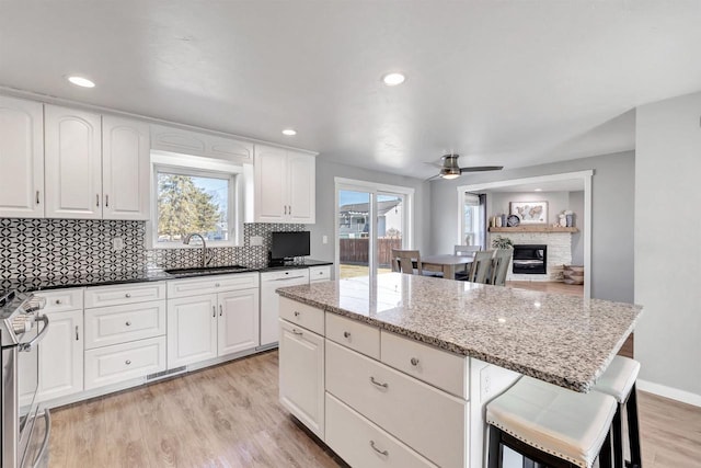 kitchen featuring light stone countertops, stainless steel range with gas stovetop, a sink, light wood-type flooring, and backsplash