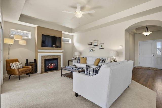 living room featuring wood finished floors, arched walkways, a fireplace, a raised ceiling, and ceiling fan