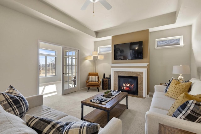 living room featuring a tiled fireplace, plenty of natural light, light colored carpet, and a raised ceiling