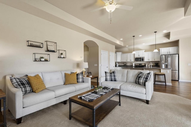 living room with baseboards, a tray ceiling, recessed lighting, wood finished floors, and arched walkways