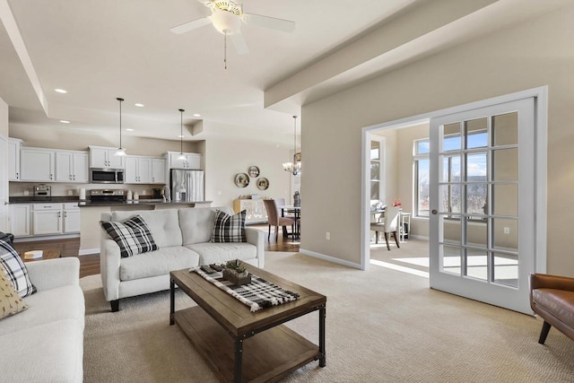 living area featuring baseboards, recessed lighting, a raised ceiling, ceiling fan with notable chandelier, and light colored carpet