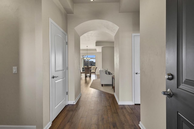 hall featuring arched walkways, baseboards, and dark wood-style flooring