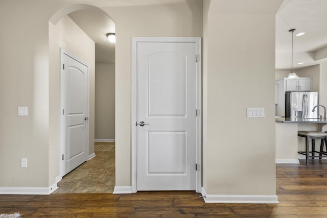 hallway featuring arched walkways, baseboards, and dark wood-style flooring