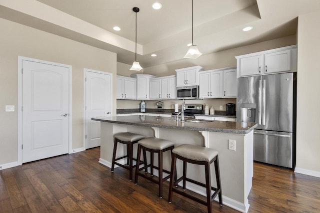 kitchen featuring stainless steel appliances, a raised ceiling, a kitchen island with sink, and dark wood-style flooring