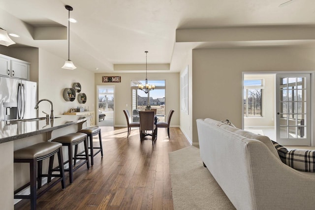 interior space with a raised ceiling, a notable chandelier, baseboards, and dark wood-style flooring