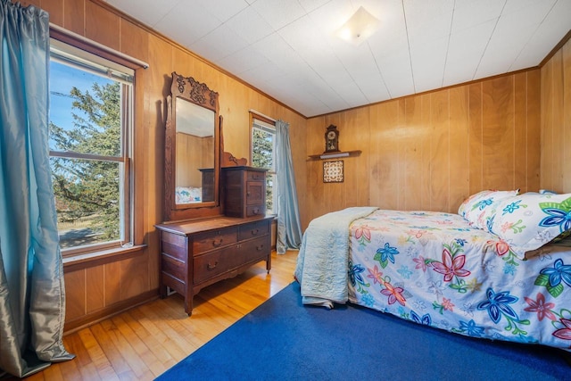 bedroom with light wood-style flooring, crown molding, and wood walls