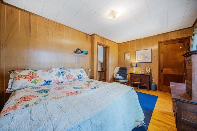 bedroom with crown molding, wooden walls, and light wood-style floors