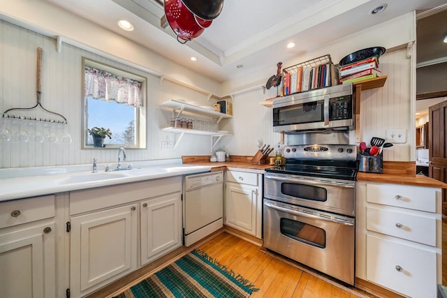 kitchen featuring open shelves, a sink, light wood-style floors, appliances with stainless steel finishes, and a raised ceiling