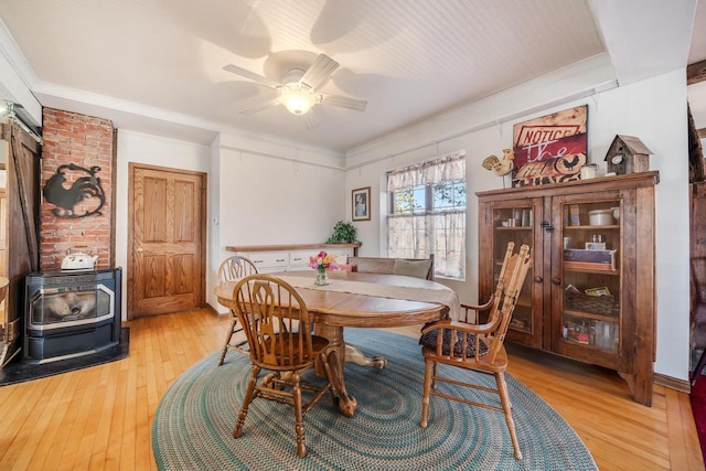 dining area with ceiling fan, a wood stove, wood-type flooring, and ornamental molding