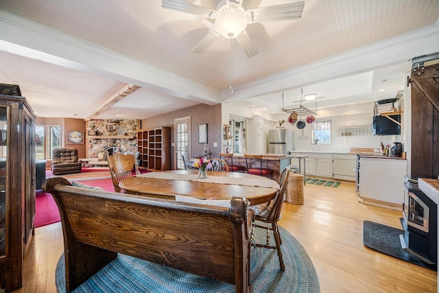 dining space with a stone fireplace, plenty of natural light, a ceiling fan, and light wood-style floors