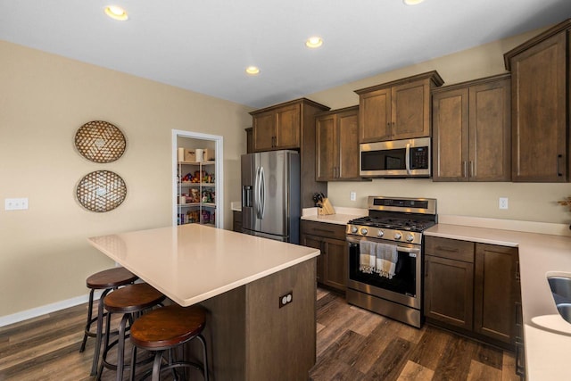 kitchen with dark brown cabinets, a center island, dark wood finished floors, a kitchen bar, and stainless steel appliances