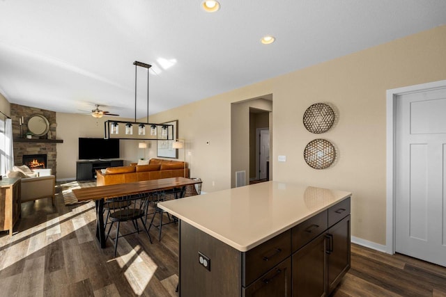 kitchen with dark wood-style floors, a fireplace, dark brown cabinetry, light countertops, and a center island