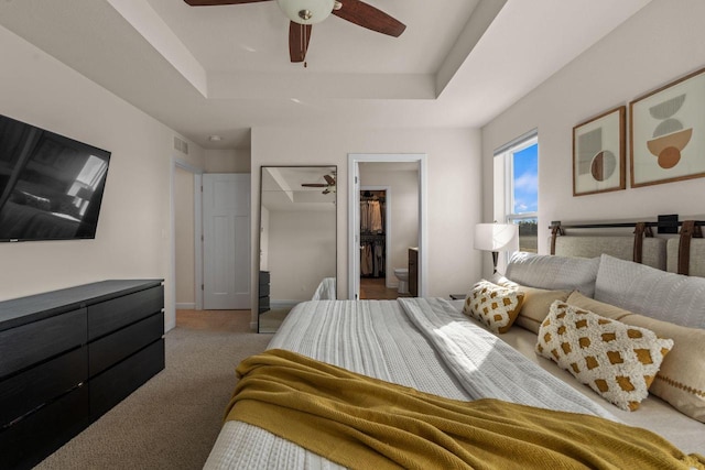 carpeted bedroom with visible vents, a ceiling fan, a tray ceiling, baseboards, and a spacious closet