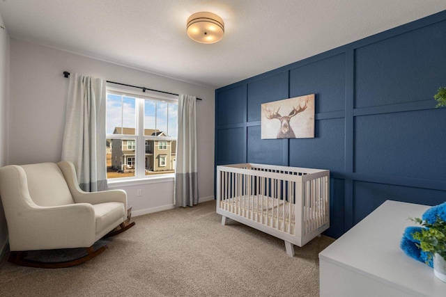 bedroom with baseboards, a crib, light colored carpet, and a decorative wall