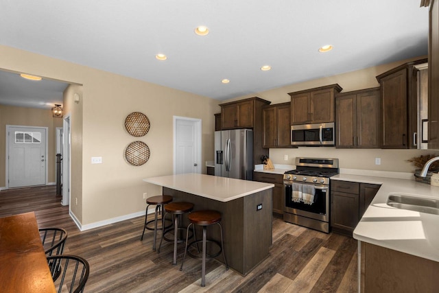 kitchen featuring a kitchen island, dark brown cabinetry, a kitchen breakfast bar, stainless steel appliances, and a sink