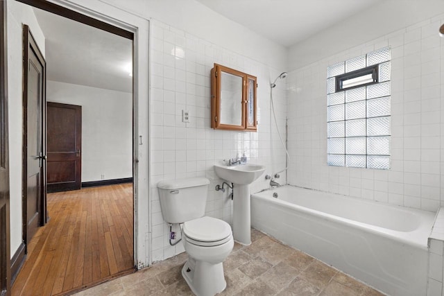 bathroom with toilet, tile walls, shower / bathtub combination, and a sink