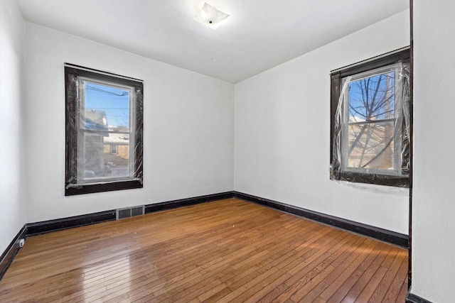 unfurnished room featuring visible vents, a healthy amount of sunlight, and hardwood / wood-style floors