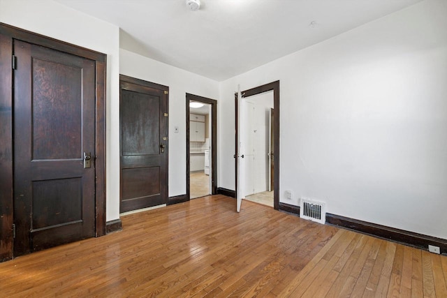 unfurnished bedroom featuring ensuite bath, light wood-style floors, visible vents, and baseboards