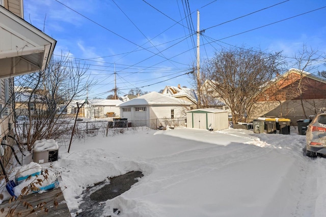 yard layered in snow with an outbuilding, a storage unit, and fence