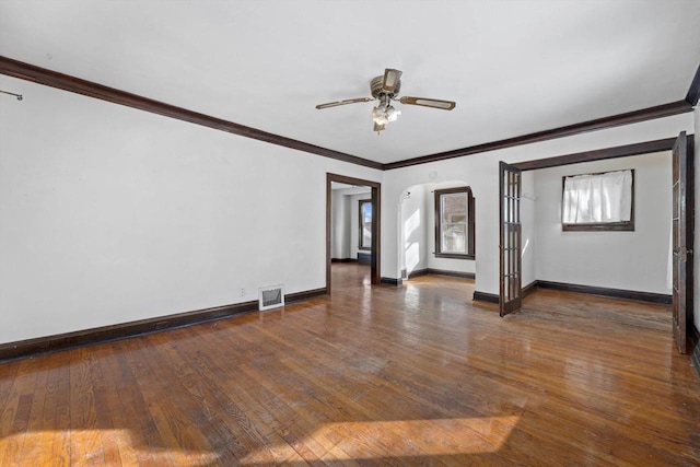 empty room featuring visible vents, hardwood / wood-style flooring, arched walkways, baseboards, and ceiling fan