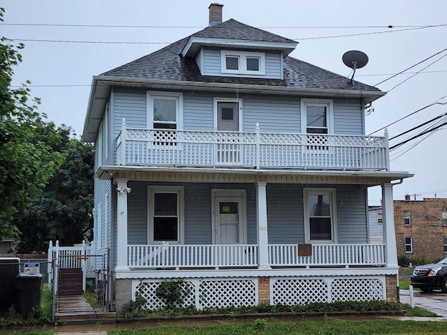 american foursquare style home featuring a porch, a shingled roof, a balcony, and fence