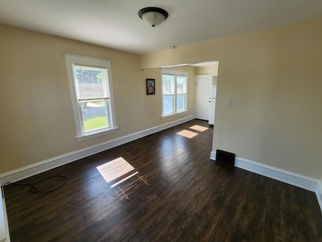 spare room with visible vents, plenty of natural light, baseboards, and dark wood finished floors