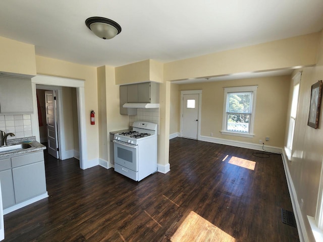 kitchen with gray cabinetry, a sink, under cabinet range hood, light countertops, and white gas range